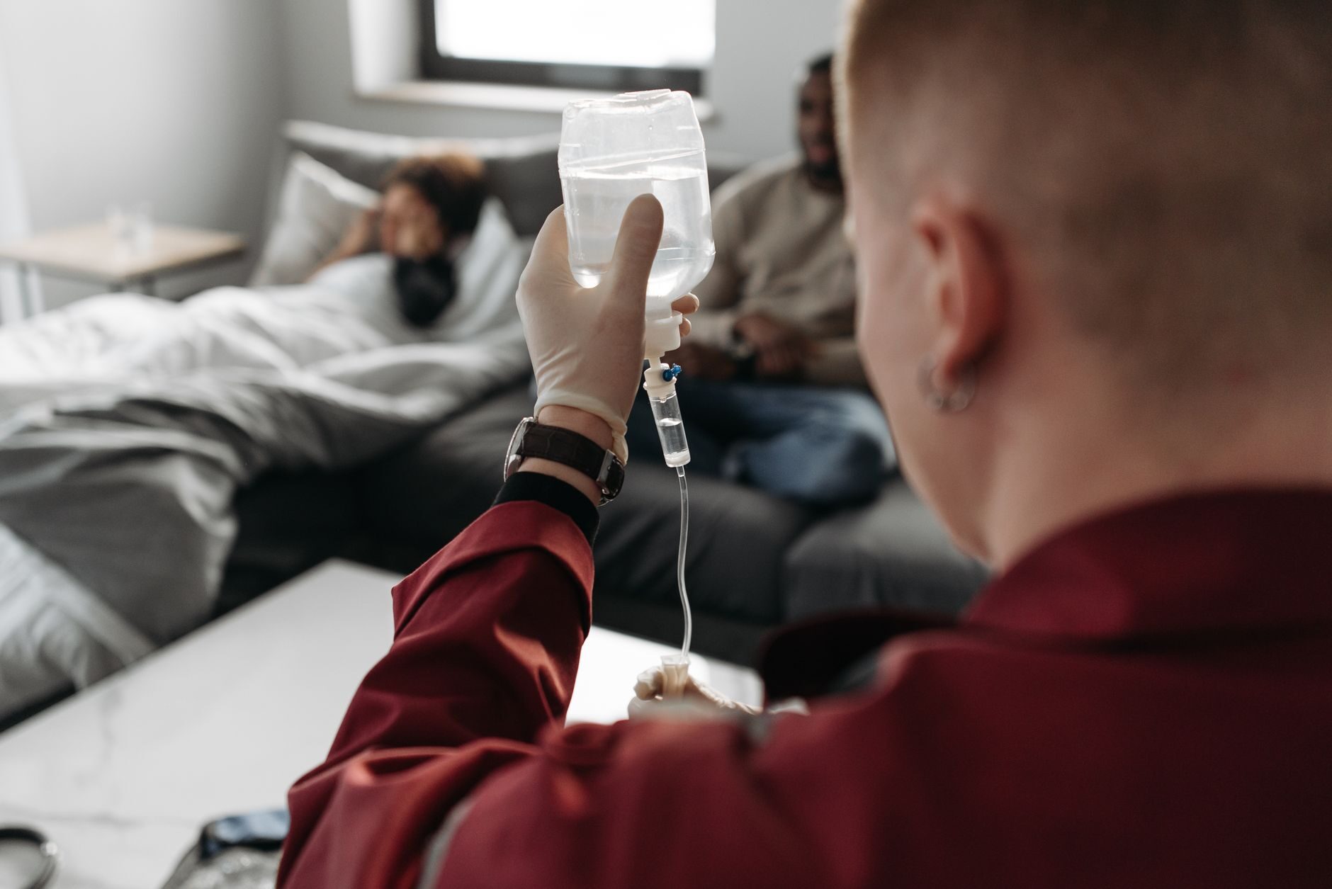 A nurse raising an IV drip bag in a relaxed living room as a client rests on the couch
