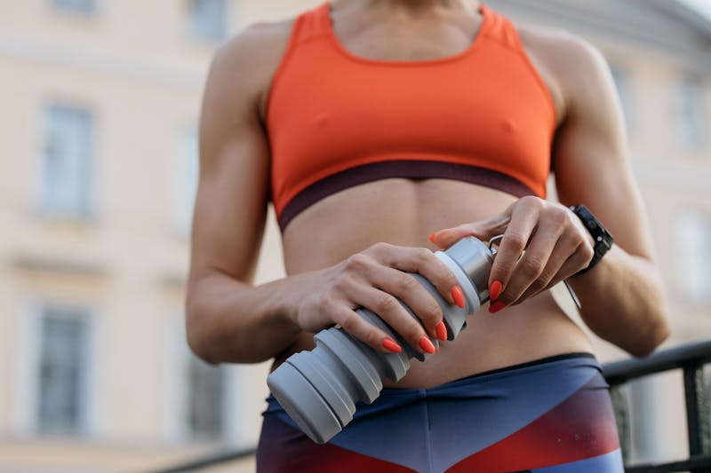 An athletic woman in a coral sports top gripping an insulated hydration tumbler