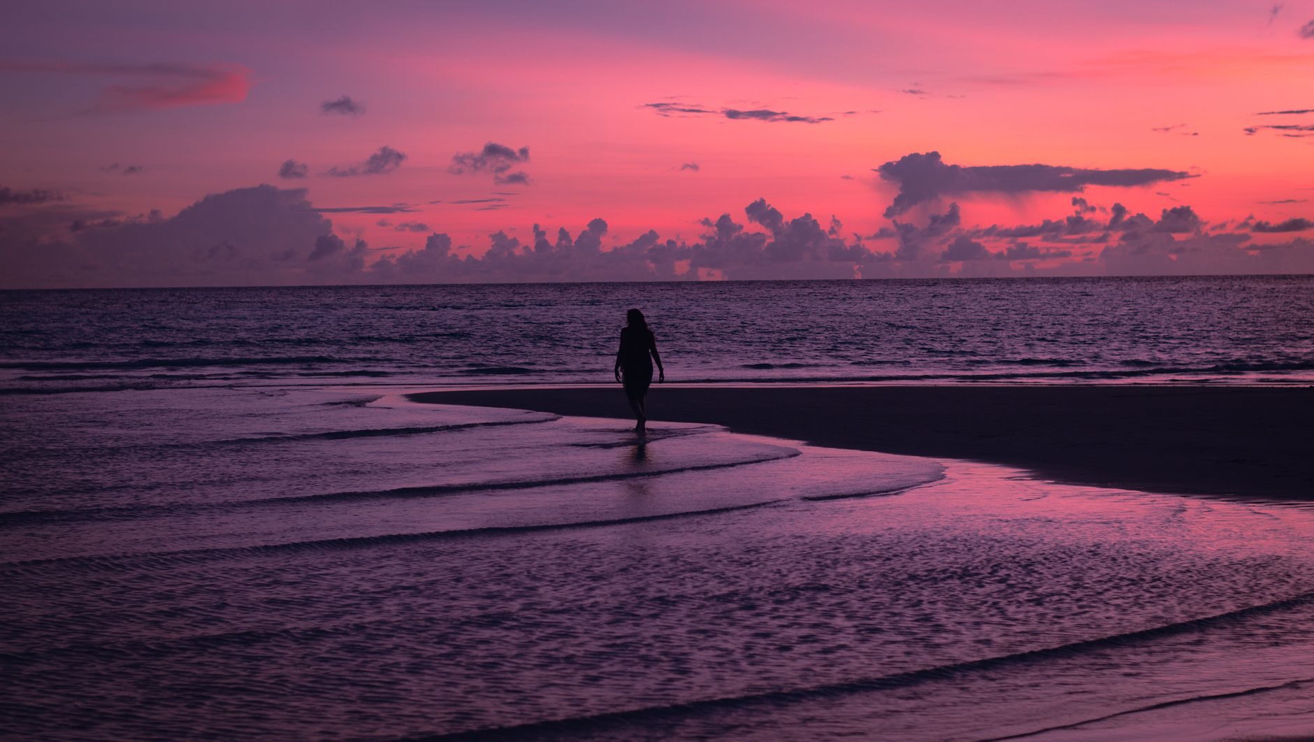 A lone woman silhouetted on a Gulf shoreline against a vivid pink-magenta sunset